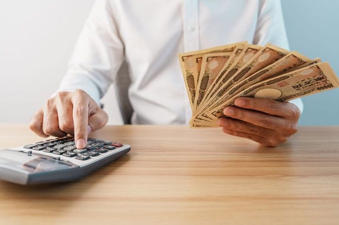 複数の一万円札を片手に、電卓を使用する男性の手元