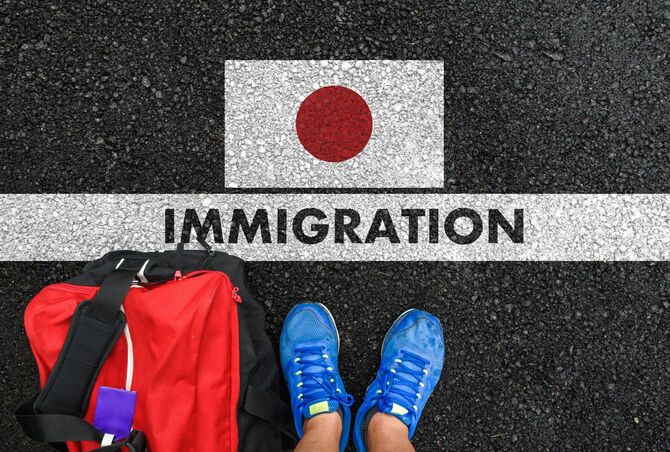 日本の国旗の下に書かれた「IMMIGRATION」の文字の前に立つ人