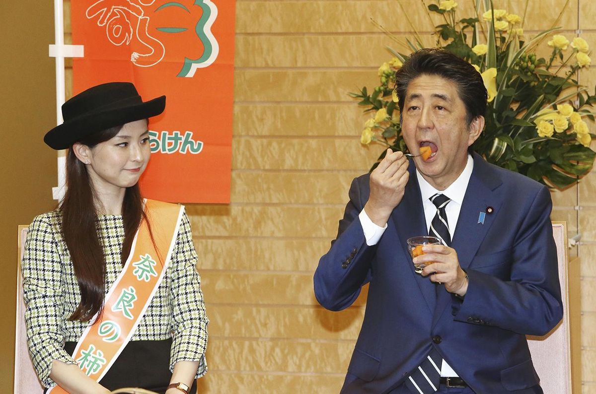 奈良県産の柿を試食する安倍首相。左は「奈良の柿PRレディ」の朝倉理恵さん＝2019年11月14日、首相官邸