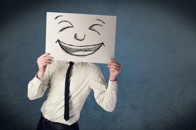 笑顔の絵が描かれた紙を自分の顔の前に持つ人