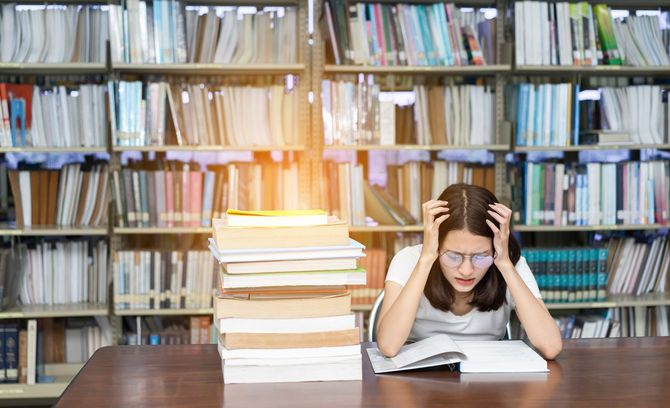 図書館で積み上げられた本の横で頭を抱えている女性