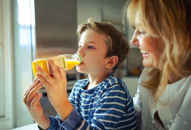母親の隣でオレンジジュースを飲む子ども