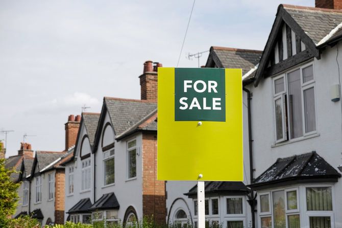 イギリスの郊外の住宅地に「For Sale」の看板を掲げた家。