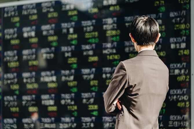 電光掲示板に表示された多数の銘柄に陳列された株価ボードを見る男の背中