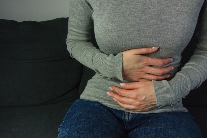 ソファに座って胃の痛みを抱える女性
