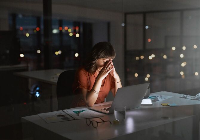 夜にオフィスでラップトップで作業している間にストレスを感じている若いビジネスウーマンのショット