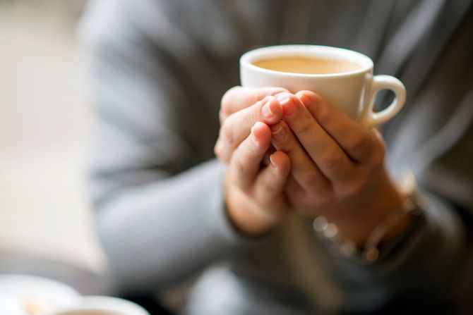 コーヒーの入ったマグカップを持つ女性の手元