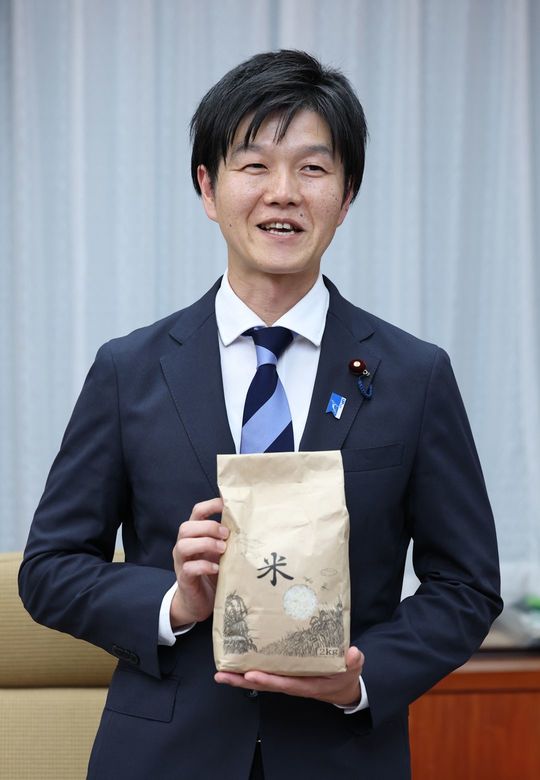 報道各社のインタビューで山形県産の「はえぬき」を手に笑顔の鈴木憲和農水相=2025年10月23日、東京・霞が関の同省