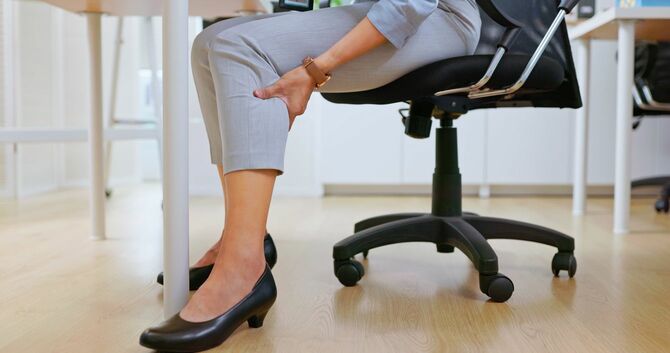 デスクチェアーで足をマッサージする女性