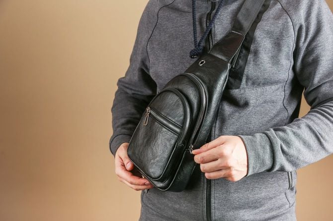 革のボディバッグのジッパーを開けている男性