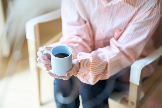コーヒーカップを持ち、椅子に座っている女性