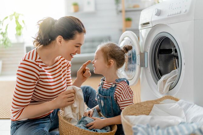 小さな娘と自宅で洗濯をしながら楽しく笑顔で過ごす若い女性