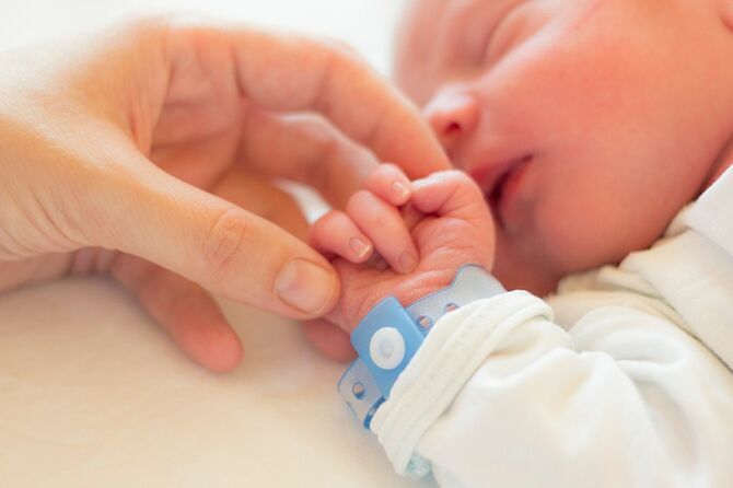 彼のベビーベッドで眠っている生まれたばかりの男の子、彼の小さな手を握って彼の母親の手。