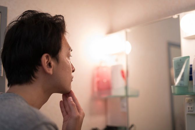洗面所で鏡を見ながらケアをする男性