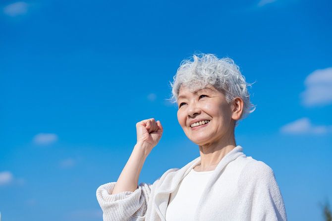 青空の下でガッツポーズをとる高齢女性