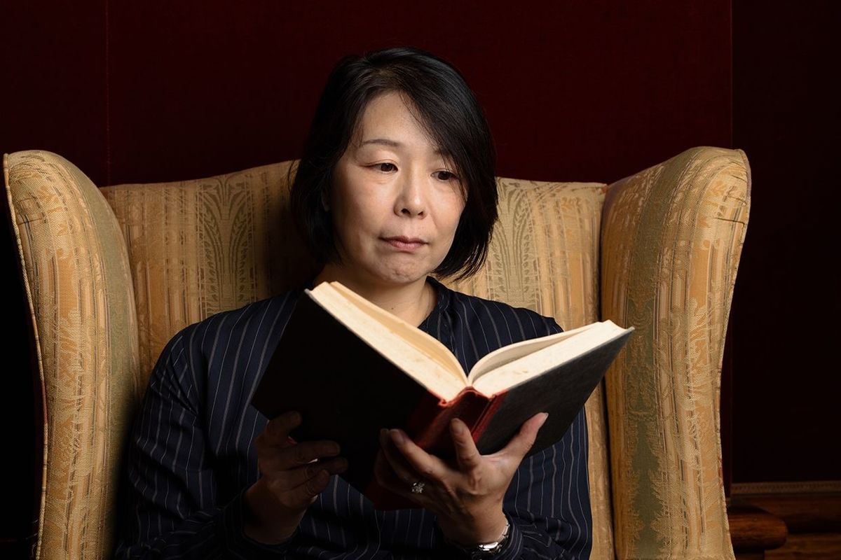 大きな古い椅子にハードカバーの本を読んでいるアジアの女性
