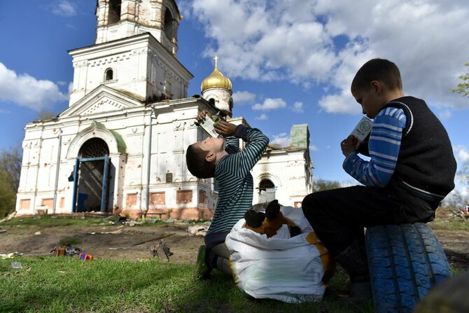 ウクライナ軍がロシア軍から奪還したチェルニーヒウ州南方の村ルカシウカで、破壊された古い教会の前でジュースを飲む子供たち（2022年04月27日撮影）