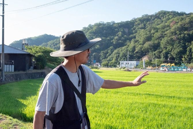 田万里について語る井本喜久さん。左手の黒い建物が田万里家