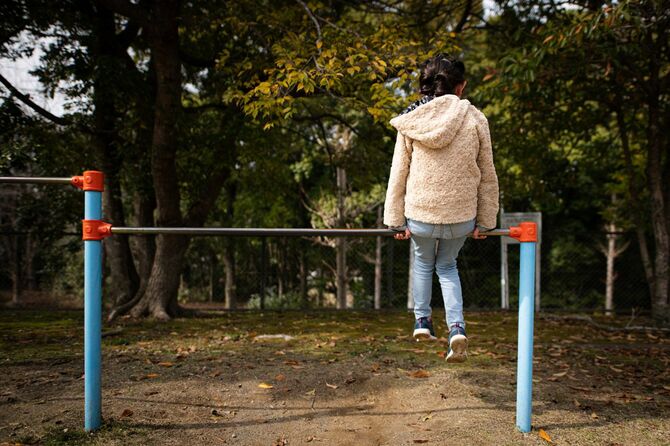 公園の鉄棒にひとりで座っている少女