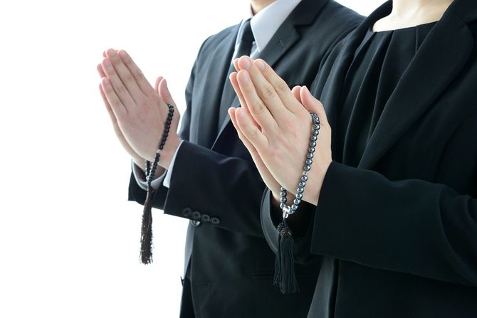 喪服を着て数珠を持つ手を合わせる人