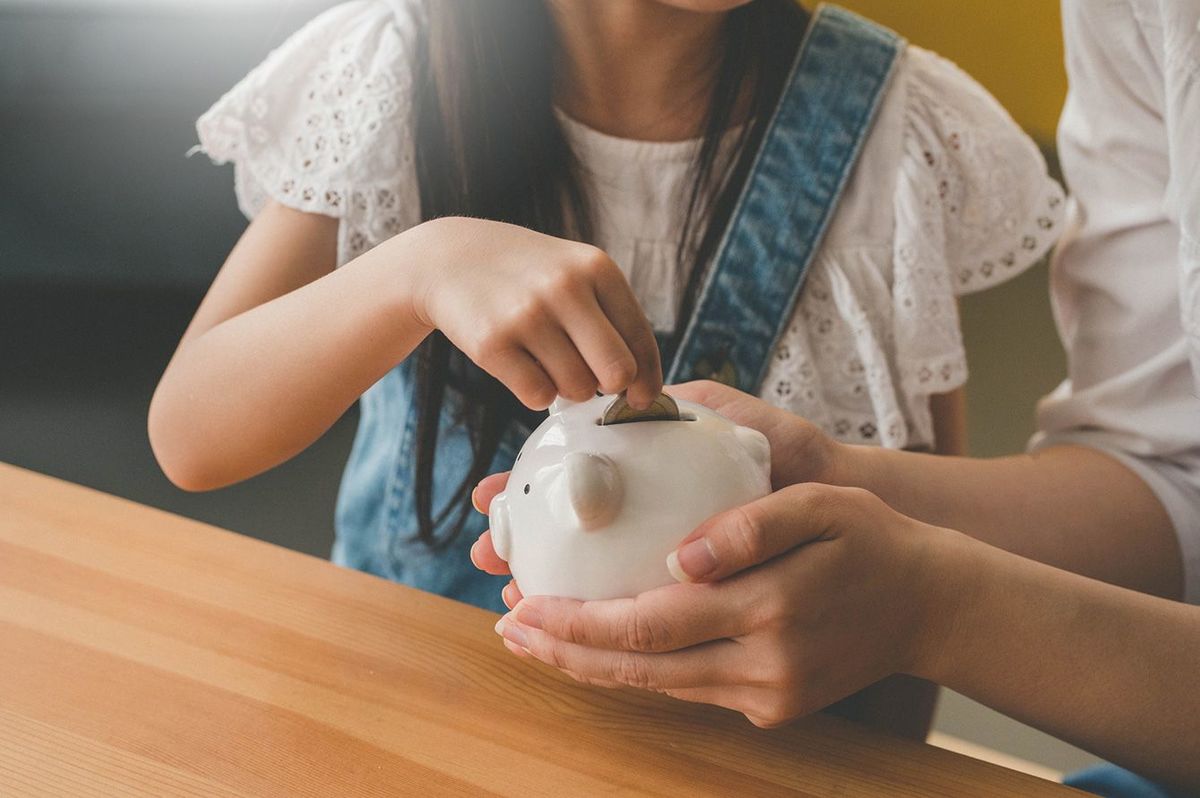 母親が手に持っている貯金箱にお金を入れる女の子