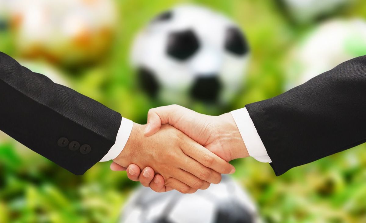 サッカーボールを背景に握手する2人のビジネスマン