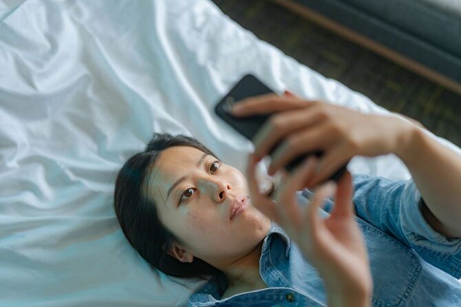 ベッドに横たわりスマートフォンを使用している女性