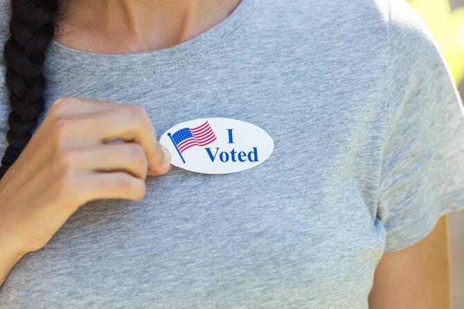 投票したことを示すステッカーを胸の前で持つ女性