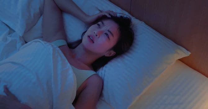 ベッドの上で眠れずにいら立っている女性
