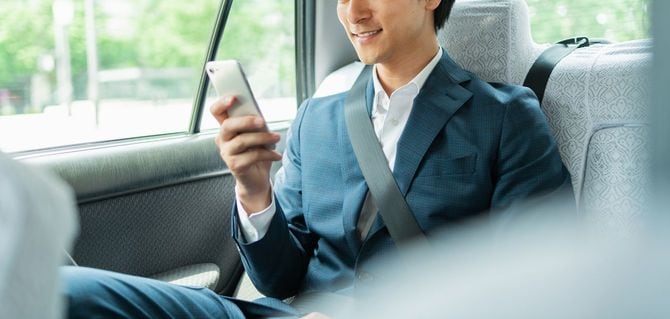 タクシーの後部座席で、スマホを見てほほ笑んでいる男性