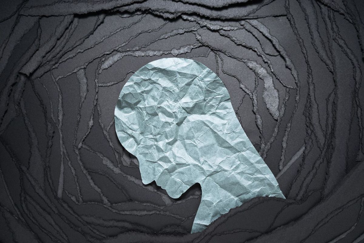 ネガティブな感情イメージ。黒い破れた紙の背景に人頭の形をした紙。