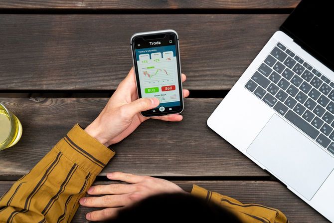 スマホの株取引アプリのチャートを見ながら「売る」「買う」ボタンのどちらを押すか迷う指先