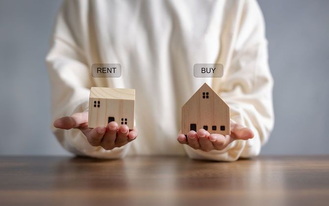 両方の手のひらに載せた家の模型と、「RENT」と「BUY」の文字