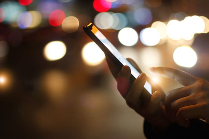 色鮮やかに光る夜道を背景にスマートフォンを操作する女性の手
