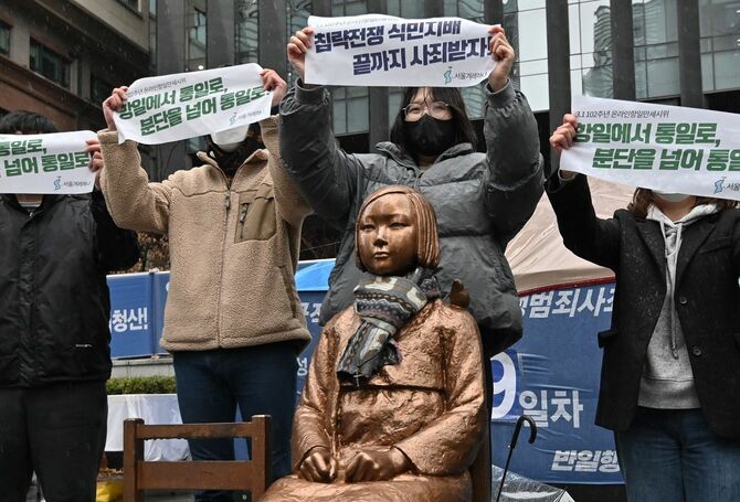 日本の「植民地支配」に反対する独立運動記念日の102周年にあたる2021年3月1日、ソウルの日本大使館近くで、第2次世界大戦中に日本兵の「性奴隷」として働いたとされる「慰安婦」を象徴する10代の少女の像のそばで横断幕を掲げる韓国のデモ隊。