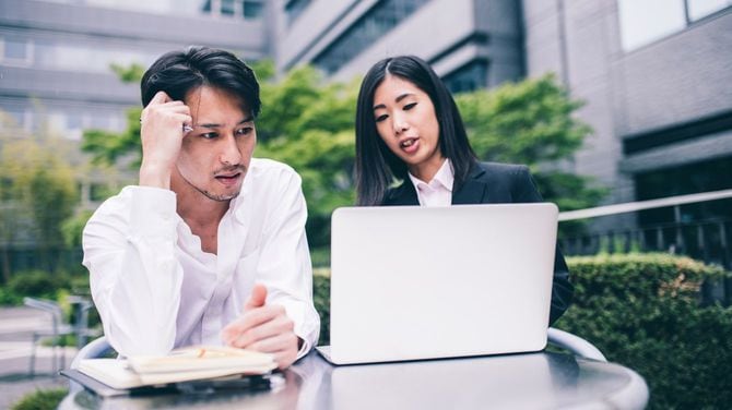 屋外でノートパソコンを開き、議論する2人のビジネスパーソン