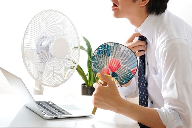 扇風機の横でラップトップを使っている日本人のビジネスマン