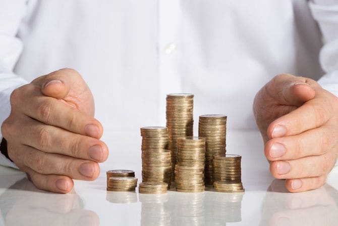 オフィスデスクで積み重ねられたコインを保護するビジネスマン