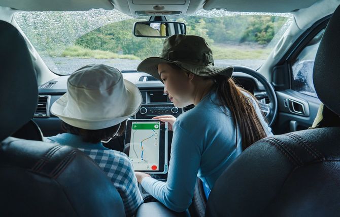 停車した車の中で子供に地図を表示したタブレット端末を見せている母親