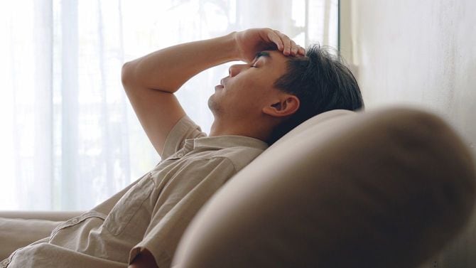 ソファにもたれて頭に手を当てている男性