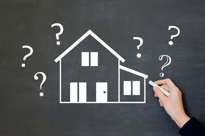 黒板に描かれた人間の手描きの家のイラストと疑問符