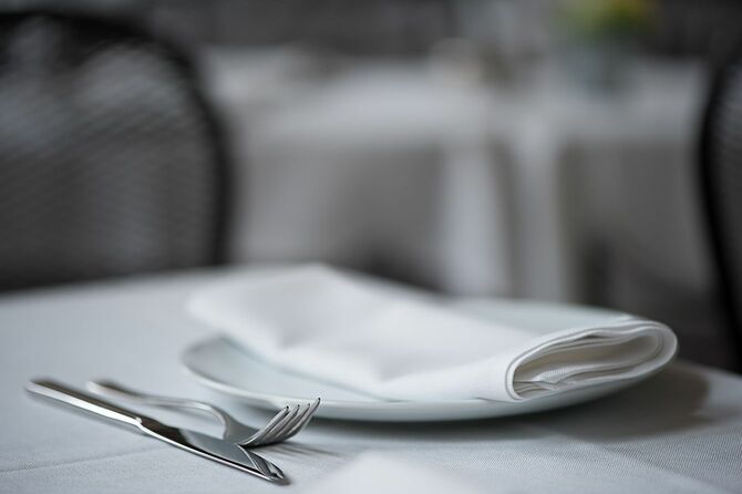 エレガントなレストランで白いテーブルクロスの上に置かれたナイフ、フォーク、プレート、折り畳まれたナプキン