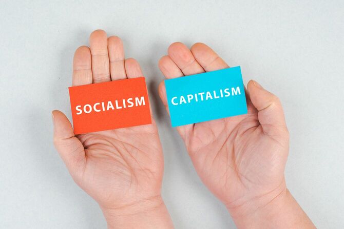 社会主義と資本主義と書かれたカードを左右それぞれの手に持っている
