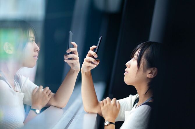 若い女性が窓でスマートフォンを使い、一人で深く考えている