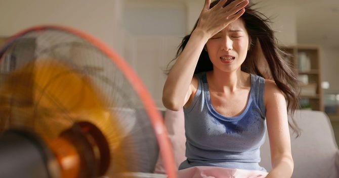 暑さに苦しみながら扇風機を使用する女性