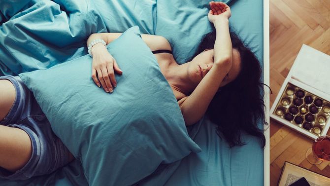 家のベッドの上で体調の悪そうな若い女性が額に腕をのせている