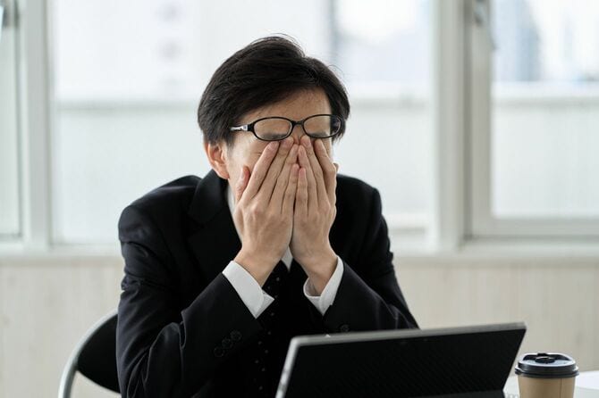 疲れ切っていて、眼鏡を押し上げて目をもんでいるビジネスパーソン