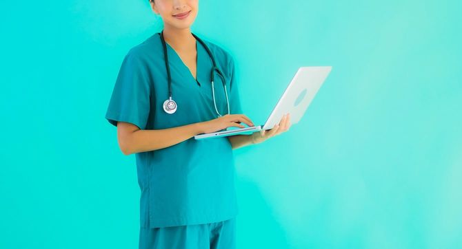 ノートパソコンを手にもって立つ女性医師