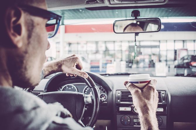  運転しながらコーヒーを片手にガソリンスタンドに向かう男