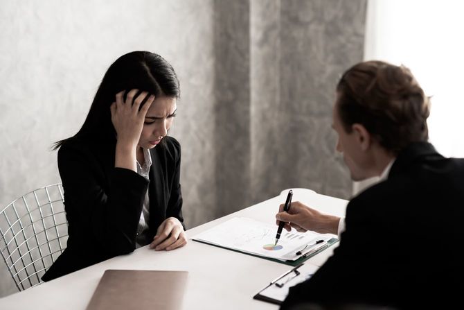 黒いスーツを着た若いビジネスウーマンはストレスを感じている。上司は、暗いトーンでオフィスの仕事の机で苦情を言います。ビジネスストレスと仕事の問題の概念。